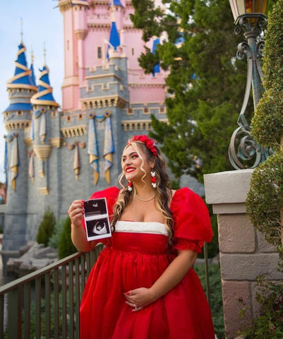 A mom-to-be poses in a princess dress holding a sonogram photo to announce her pregnancy at Disney