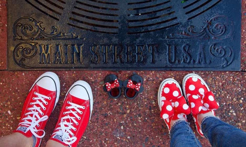 A Disney pregnancy announcement with two adults posing in red shoes next to a pair of child-sized Minnie Mouse shoes