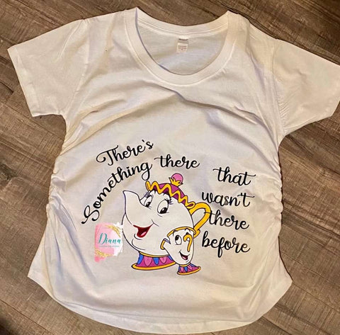 A pregnancy announcement t-shirt that says "there's something that wasn't there before" with an illustration of Mrs. Potts from Beauty and the Beast