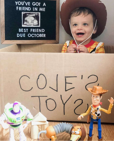 Disney pregnancy announcement photo: A toddler dressed as Woody from Toy Story poses in a box next to a sign that says "You've got a friend in me best friend due October" 