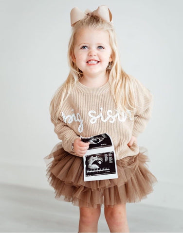 DIY pregnancy announcement photo of a little girl wearing a "big sis" shirt and holding an ultrasound photo
