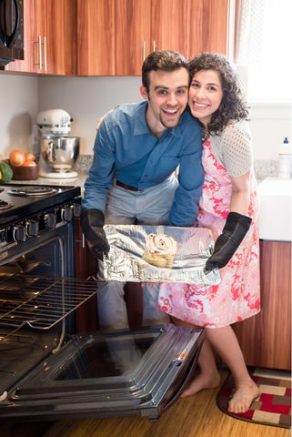 DIY pregnancy announcement photo of a couple posing with a cinnamon bun next to an oven
