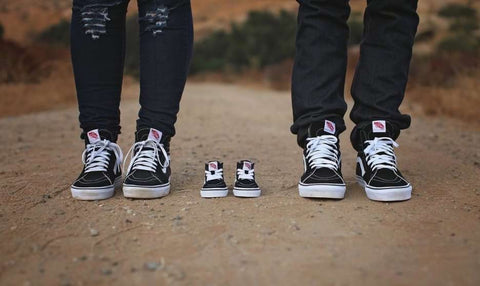 DIY pregnancy announcement photo of three pairs of sneakers: two adult pair and one pair of baby shoes