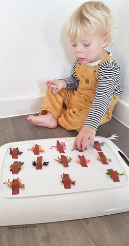 A toddler tries to "free" toy animals that have been taped down onto a tray.