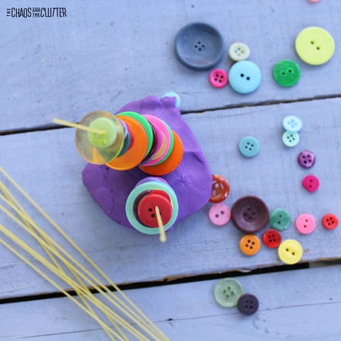 Buttons threaded and stacked on a dry spaghetti noodle that's held upright by playdough.