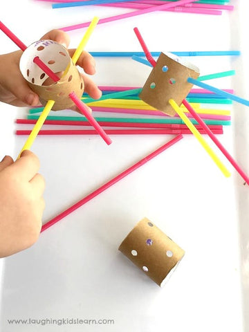 A toddler does a fine-motor threading activity with pipe cleaners and toilet paper rolls.