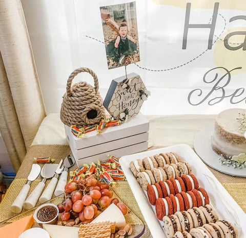 Food table for a bee-themed first birthday party that features honey candies, cookies, and a cheese plate. 