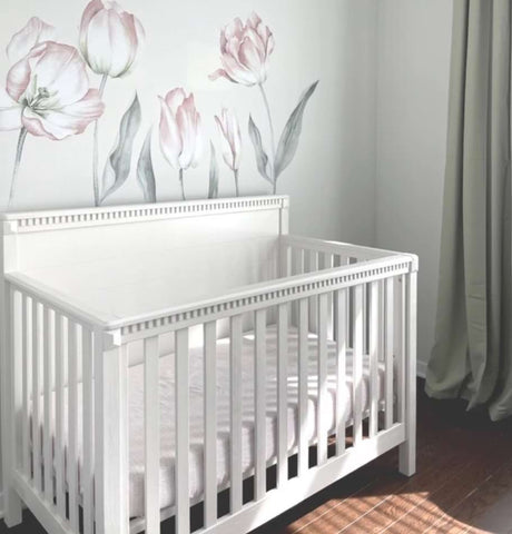 A white crib against a wall painted with tulips in a floral-themed nursery