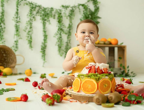 Baby eating smash cake decorated with fruit.