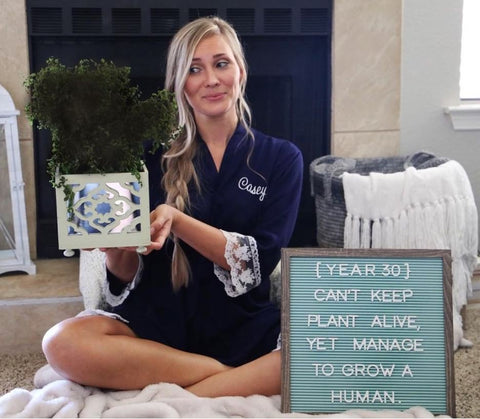 Woman poses with a plant in front of a letterboard announcing a pregnancy