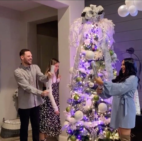 A couple opens British-style "Christmas crackers" in front of a decorated tree