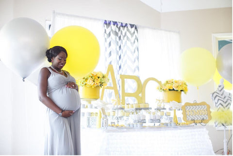 A pregnant woman poses near decor for a gray and yellow baby shower