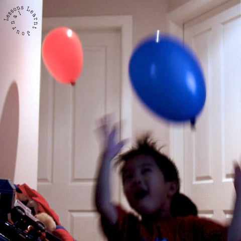 A toddler bats two balloons around his house.