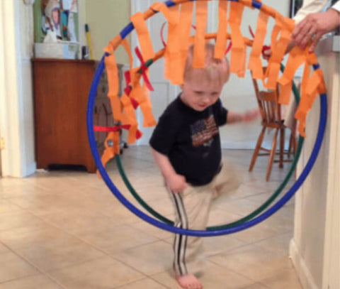 Toddler climbing through hula hoops decorated with orange streamers.