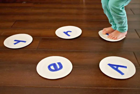 Toddler hops onto paper plates decorated with different letters.