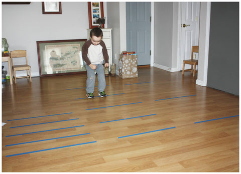 Toddler in living room jumping over tape lines on the floor.