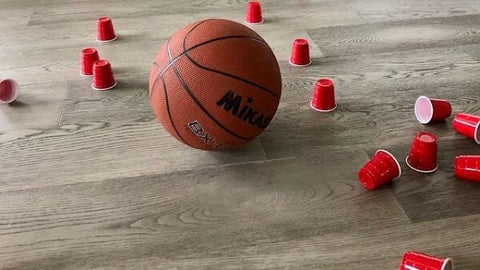 A basketball on the floor near knocked-over plastic cups after a homemade game of bowling.