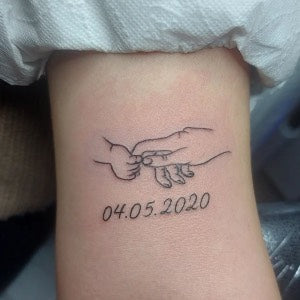 Close-up image of a wrist tattoo featuring the name and birthdate of a child in elegant script font