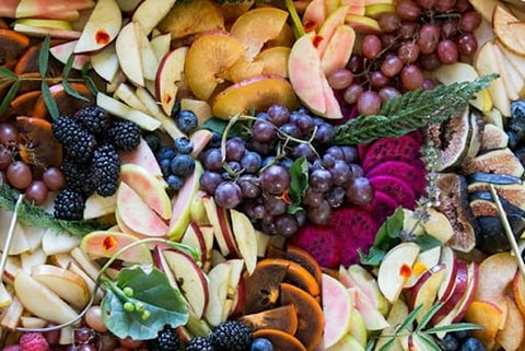 A spread of purple grapes, sliced red apples, figs, blackberries, and more for a fall baby shower