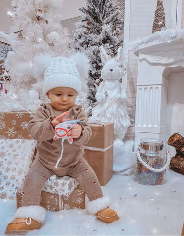 A baby poses with Christmas trees and gifts to celebrate first holiday