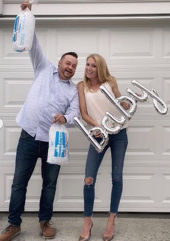 Man holding two bags of ice next to woman holding "baby" sign