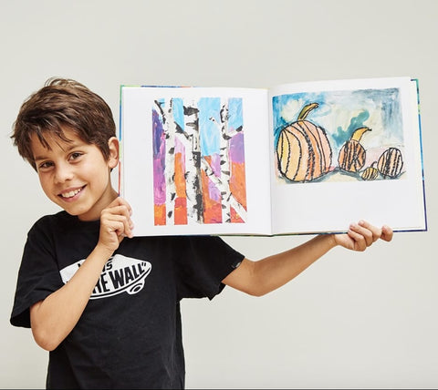 Child holds bound book of his artwork