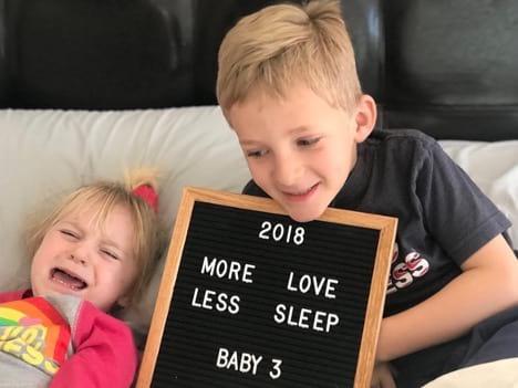 Boy holding letterboard that says "More love less sleep" next to screaming toddler