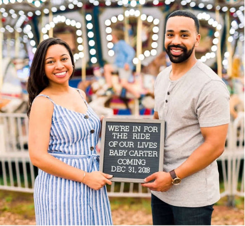 A couple poses with a pregnancy announcement letterboard at an amusement park