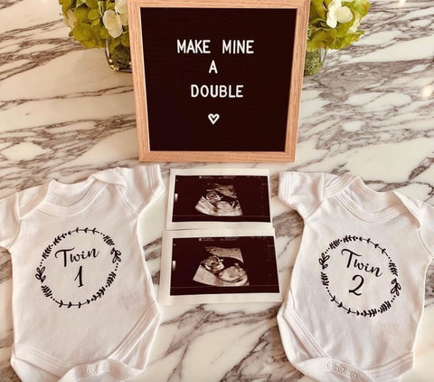 Two onesies and twin ultrasound displayed with letterboard announcing a twin pregnancy