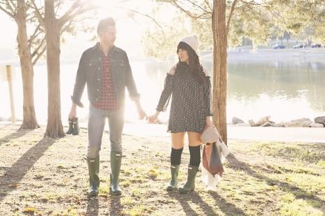 A couple wears matching Hunter boots as they hold a pair of child-sized boots to announce their adoption