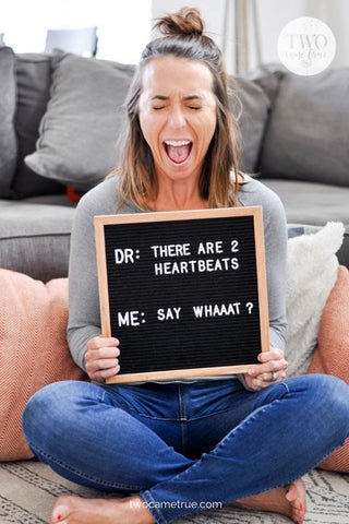 Mom holds letterboard announcing twin pregnancy with a shocked look on her face