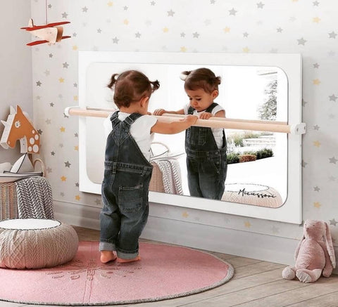 Toddler stands at child-size barre and looks in the mirror in a Montessori-style nursery