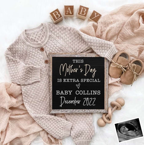 Mother's Day pregnancy announcement flat lay featuring a letterboard, blocks, and a baby romper