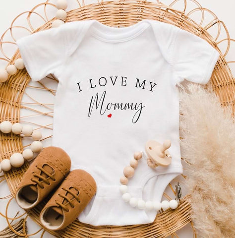 Mother's Day pregnancy announcement flat-lay featuring a onesie that says "I love my mommy"
