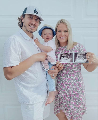 A mom, dad, and toddler pose with an ultrasound picture to announce a pregnancy on Mother's Day
