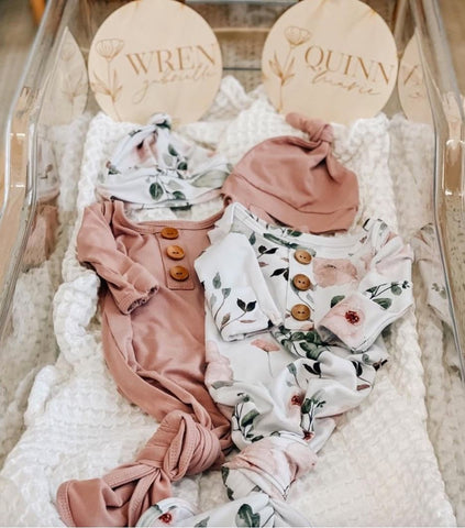 Two baby girl outfits displayed with baby girl name placards in a bassinet to announce a twin pregnancy