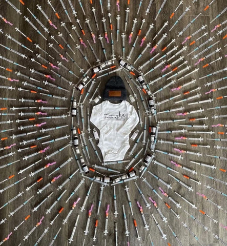 Baby bodysuit surrounded by needles to announce pregnancy