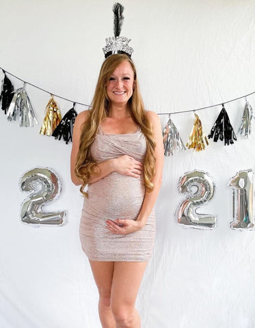 A pregnant woman poses with a 2021 sign to announce a pregnancy on New Year's