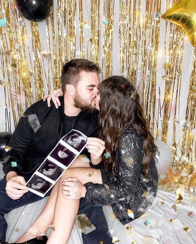 A couple poses with their ultrasound pictures at a New Year's party to announce a pregnancy