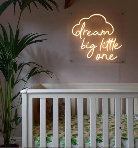 A neon sign above a crib that says "dream big little one"