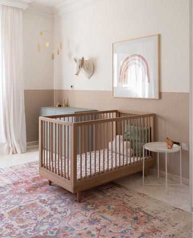 A light pink patterned Persian-style nursery rug in a baby's room