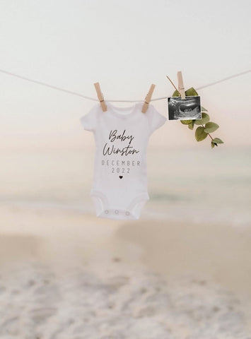 Baby onesie hanging on clothesline on a beach used to announce pregnancy
