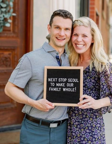 Couple holding letterboard that announces they're adopting from Seoul