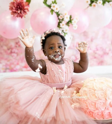 Baby in pink dress eating pink smash cake. 