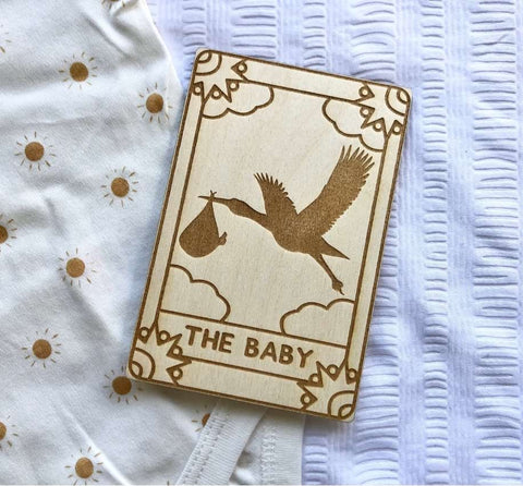 A wooden tarot card themed bookmark that says "The Baby" with an etching of a stork