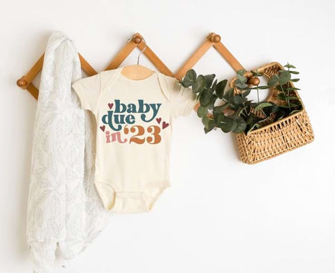 Pregnancy announcement onesie that says "baby due in '23" in colorful letters