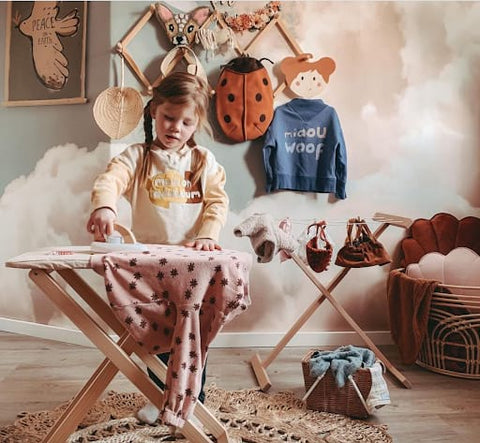 Toddler pretending to iron on a pretend ironing board in a toddler room play space.