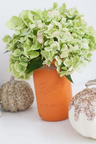 Pale green flowers in a terracotta mason jar and glittered pumpkins for a fall baby shower