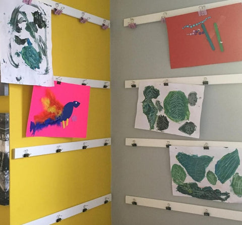 Kids' artwork displayed on magnetic strips with clips.