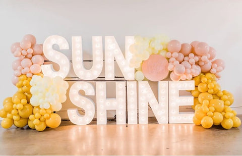 Light-up sign that says "sunshine" decorated with pink and yellow balloons for a baby shower